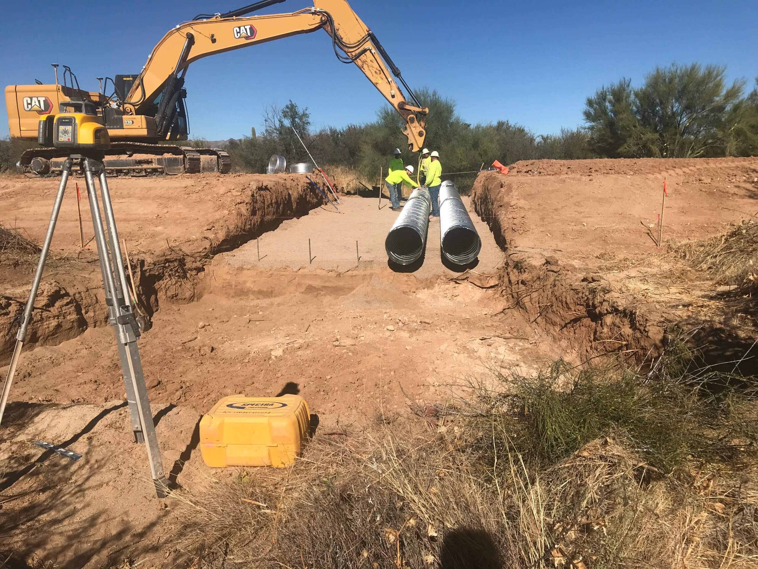 Land surveying equipment set up at a job site aimed at an excavator and pipes